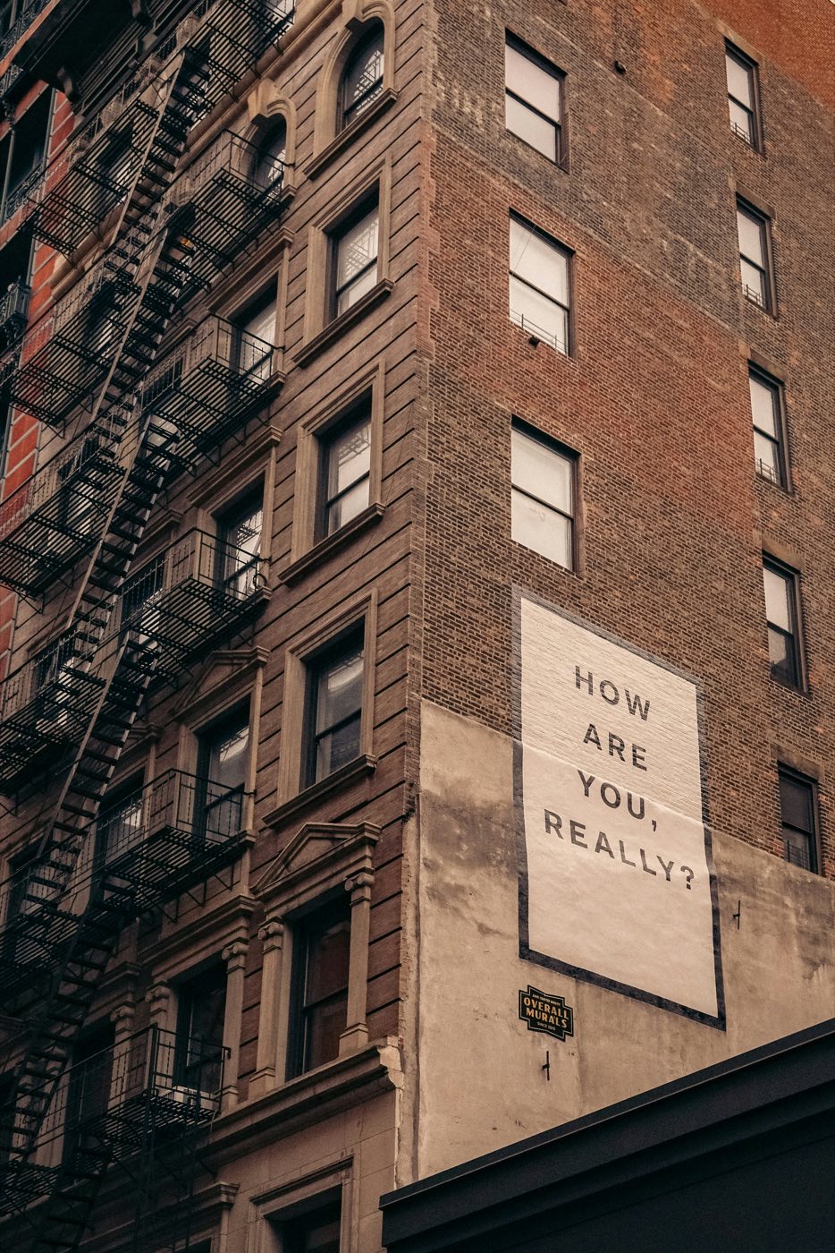 A mural pasted on a city building reading: How are you, really?